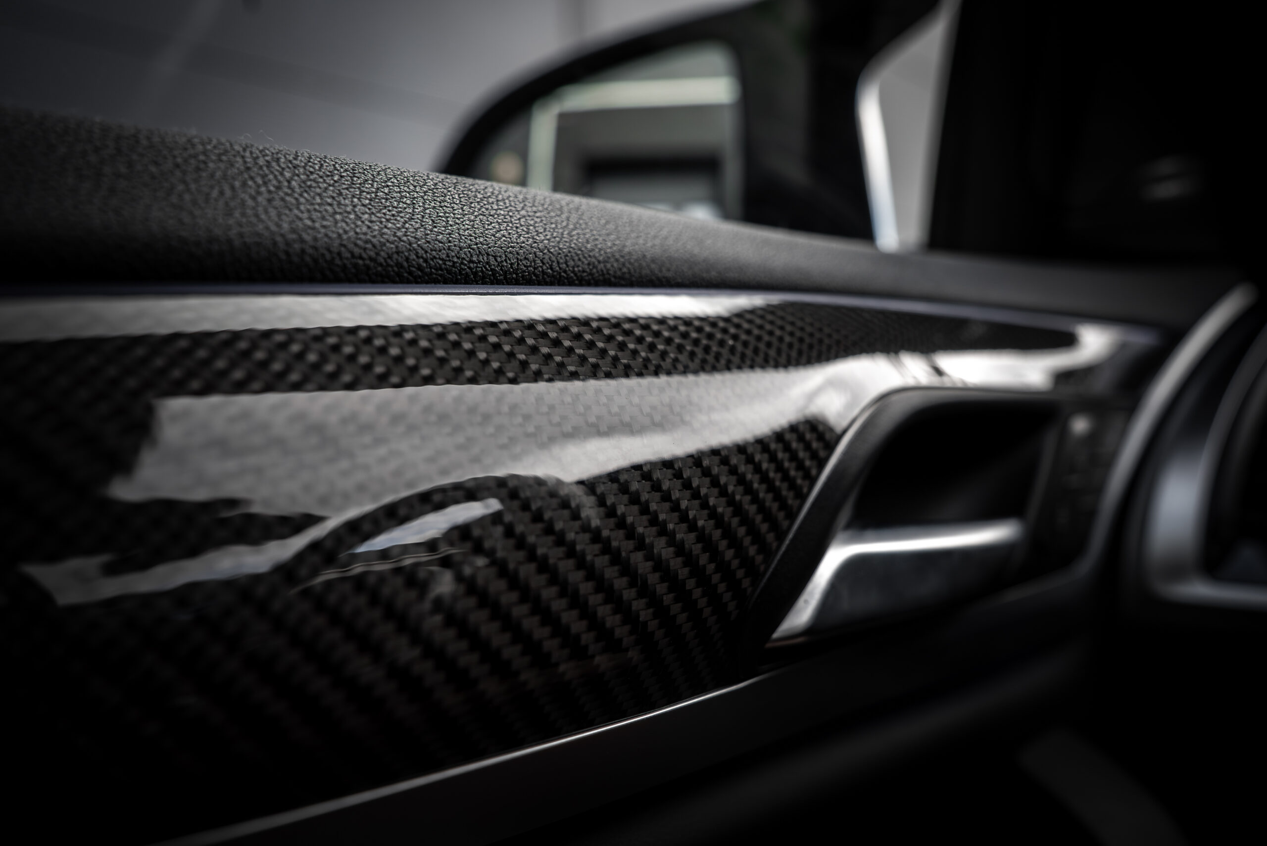 Detailed view of a BMW X4 door panel featuring carbon fiber trim, metallic handle, and textured black leather with blurred interior in the background.